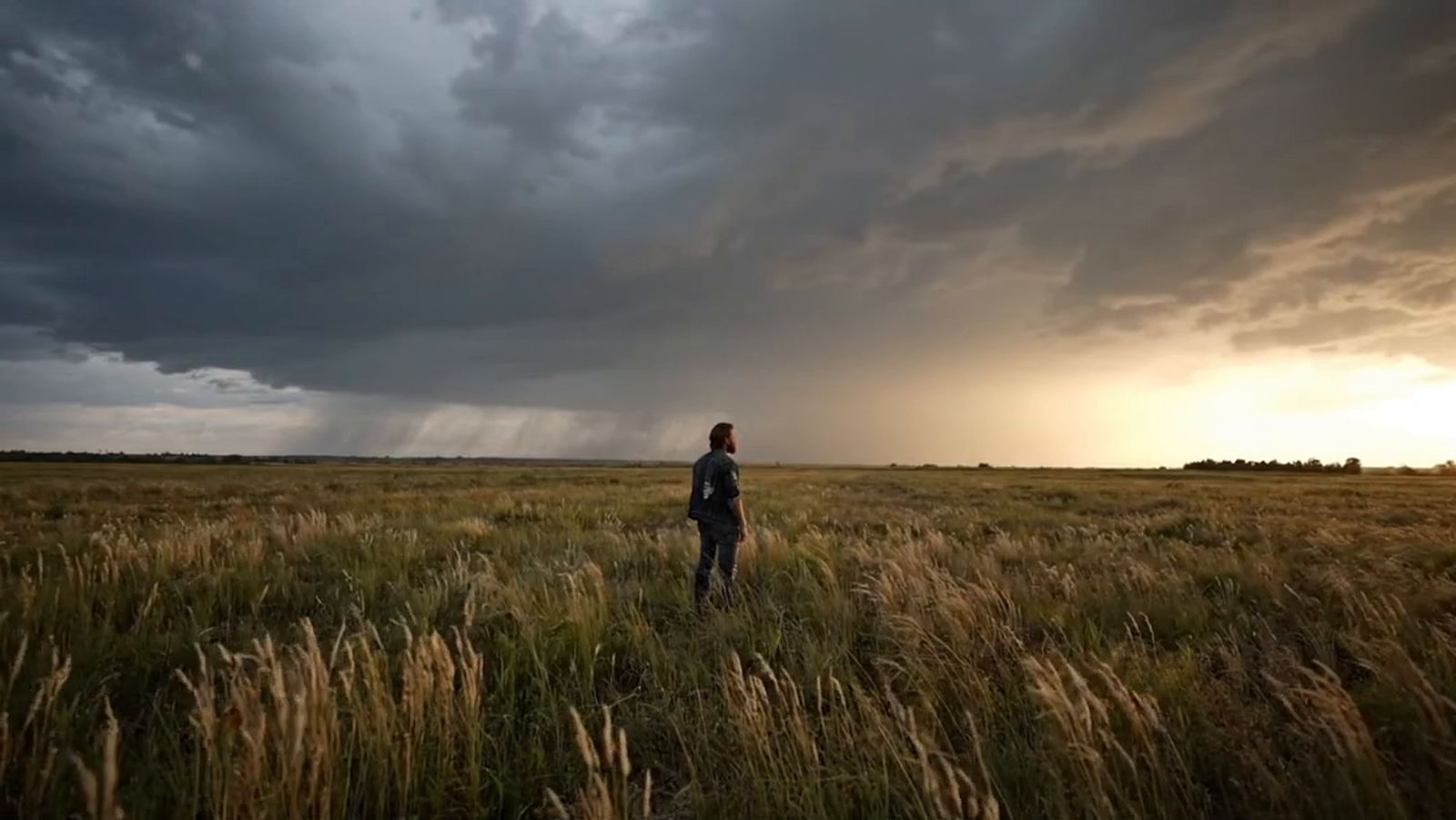 A lone man stands in a prairie under a storm sky at golden hour, from the What Will My Life Say video
